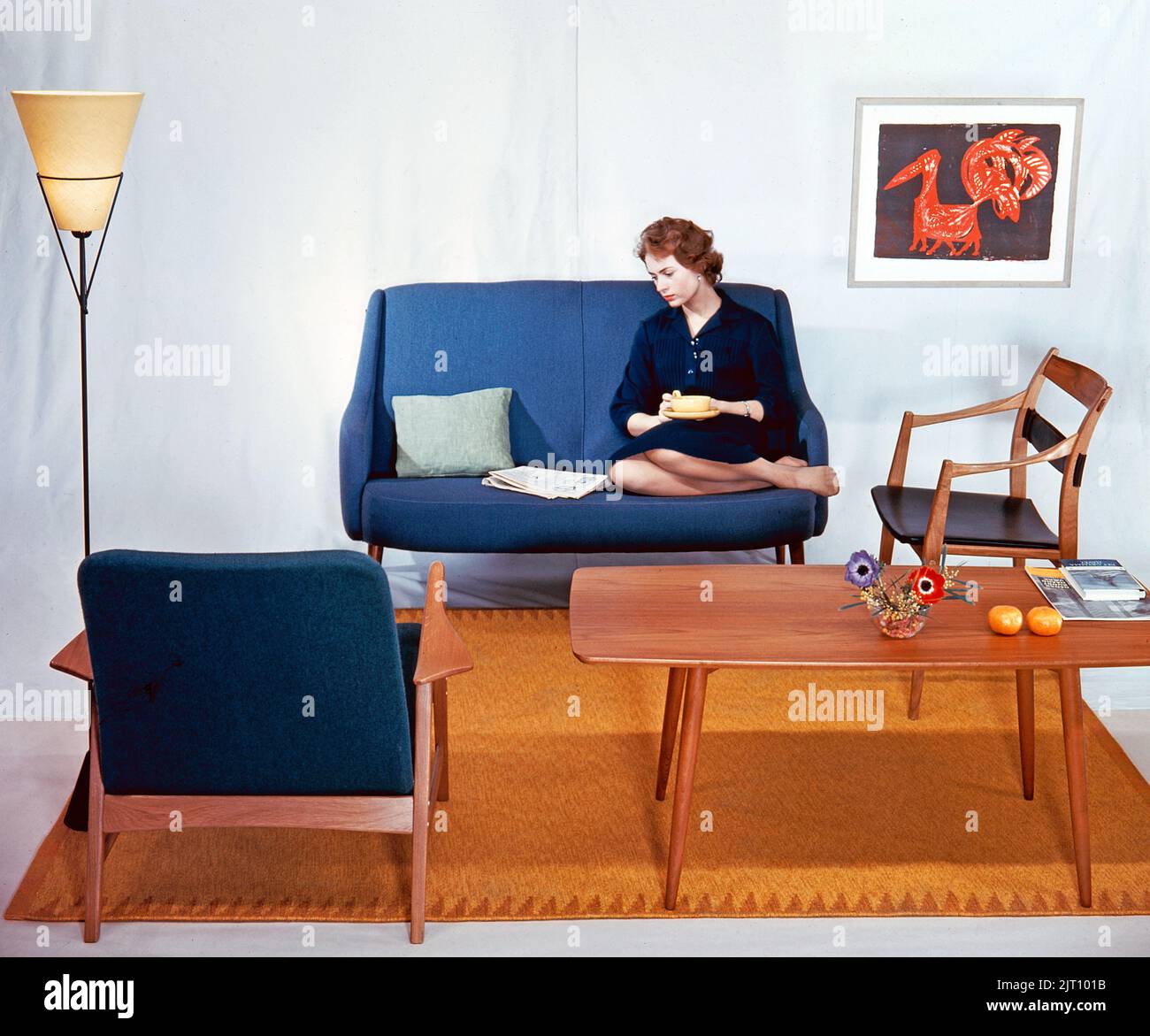 In the 1950s 1960s. A woman is sitting comfortably in a couch reading the newspaper and having a cup of tea. The furniture are made of wood and typical of the late 1950s early 1960s style.  Sweden 1958 Conard ref BV109-6 Stock Photo