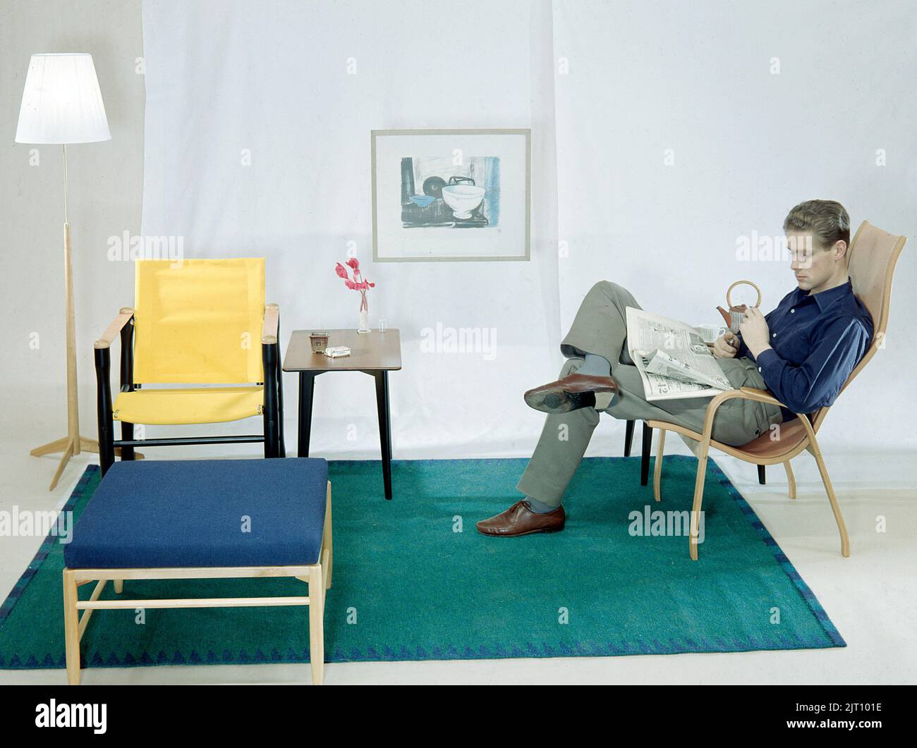 In the 1950s 1960s. A man is sitting comfortably in an armchair reading the newspaper and having a cup of tea and a cigarette. The furniture are made of wood and typical of the late 1950s early 1960s style.  Sweden 1958 Conard ref BV109-6 Stock Photo