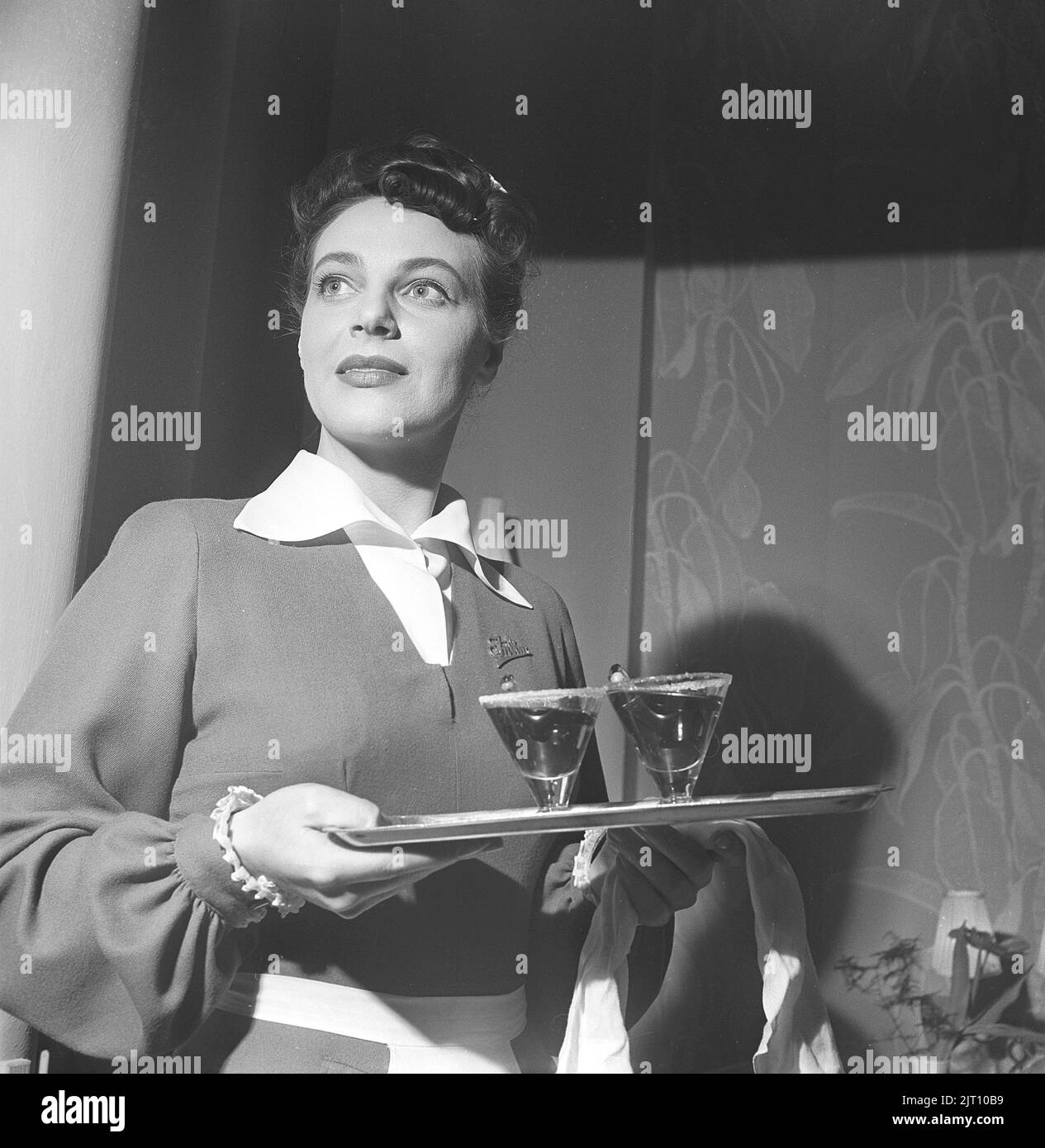 Service in the 1940s. A woman working as a waitress  in a restaurant, bar or hotel is standing ready with a tray with two drinks on it. She is nicely dressed and has beautiful hair. Sweden 1949 Kristoffersson ref AU111-2 Stock Photo