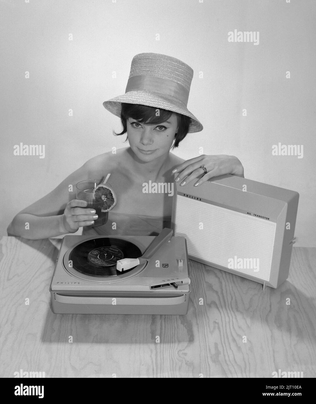1960s lifestyle. A young woman with a Philips radio and a gramophone as it could look in the summer. The summer hat and the cool drink glass is in the picture to get the right summer feeling. Sweden 1960s Photo Kristoffersson Ref 374A Stock Photo