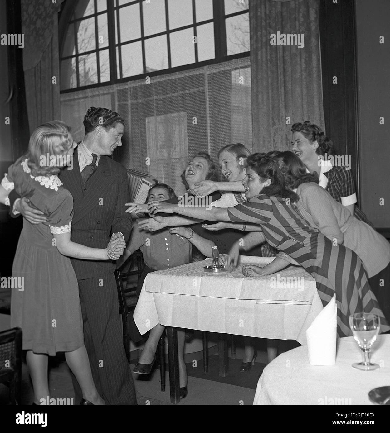 In the 1940s. Seven young women but only one man, and the six that are not dancing reaches out their arms for him. Picture taken in the town Boras where the saying is that there is a shortage of single men.  Only one free and single man on seven women.  Sweden 1942. Photo Kristoffersson ref A50-3 Stock Photo