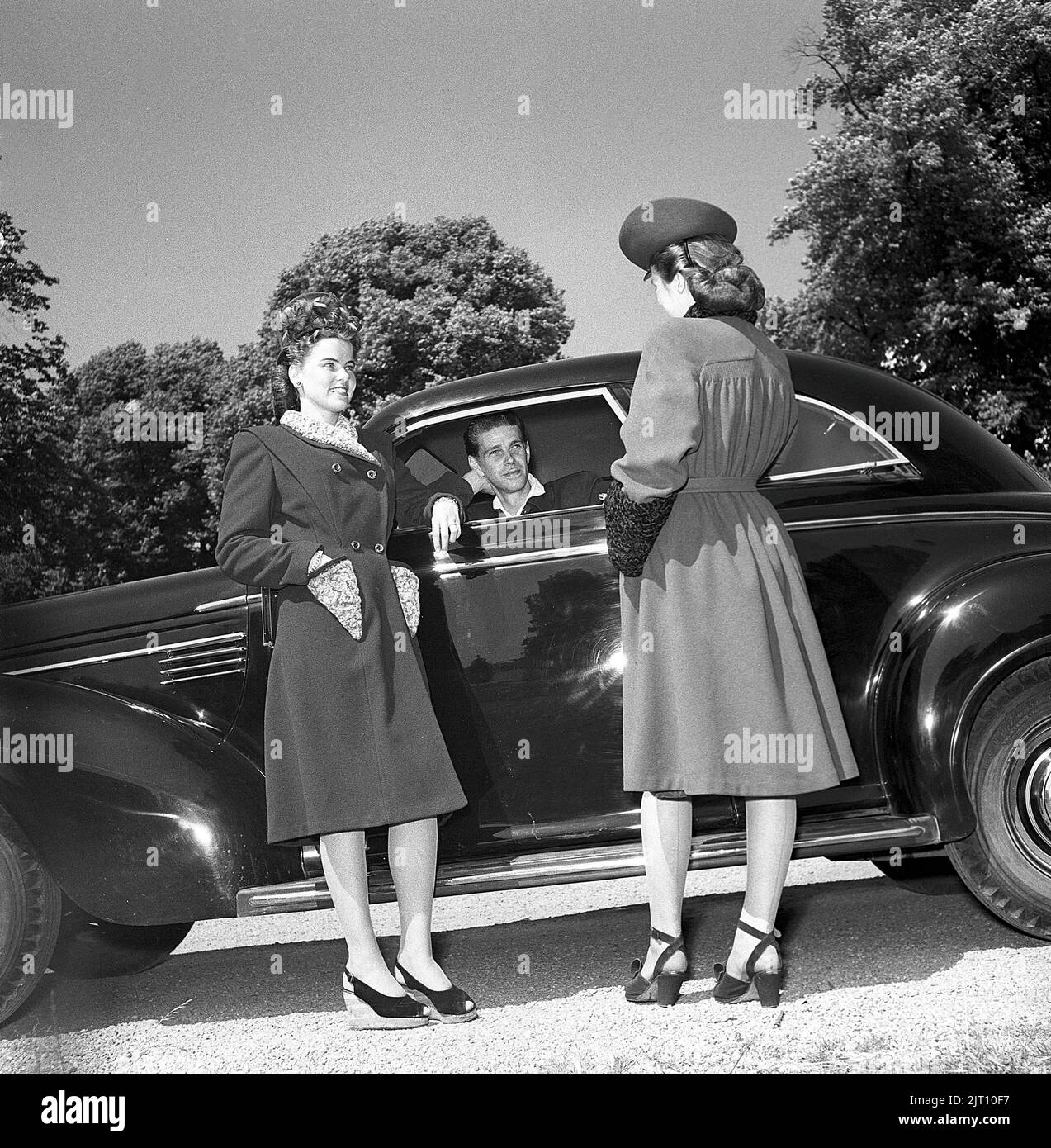Women's fashion in the 1940s. Two young women in  typical 1940s outfits. Warm coat, matching shoes and hat. They are pictured beside a car talking to the male driver. Sweden 1946. Kristoffersson Ref U128-5 Stock Photo