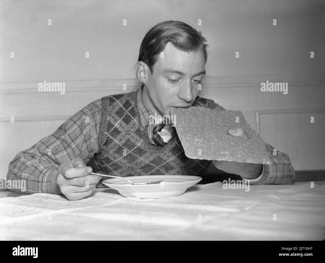 1940s meal. A young man, athlete Erik Pettersson at the food table taking a bite from the bread. He holds it like a painters palette with his thumb visible in a hole of the bread, perhaps he found the perfect way of holding it this way. Sweden 1940 Kristoffersson Ref 75-1 Stock Photo