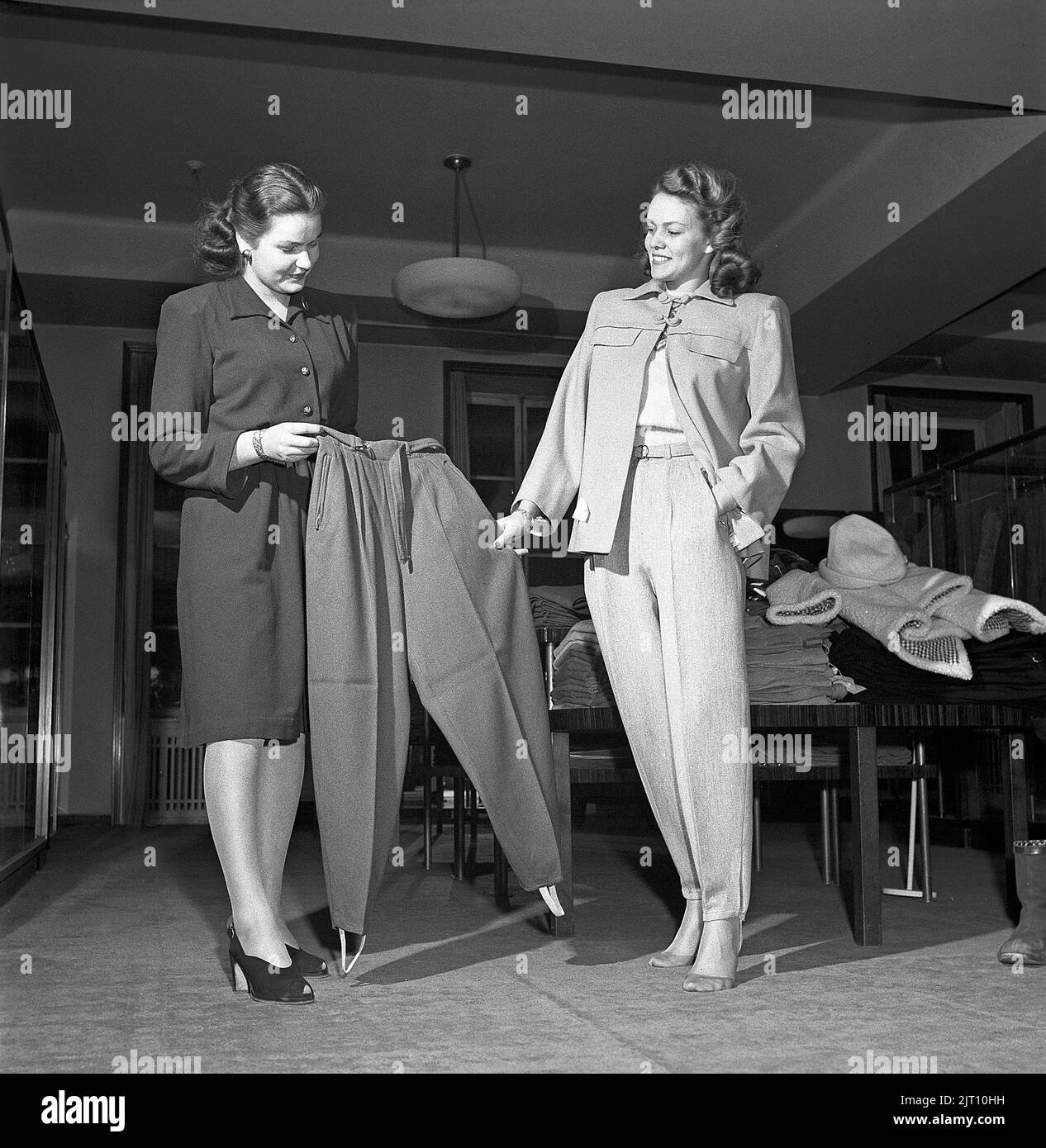 Shopping in the 1940s. A young woman in a store where a sales woman is presenting some of the stores selection of winter trousers, typically a fashion of the 1940s in a syntethic material with straps under the feets, often used when skiing but also the every day fashion of the young. Sweden 1947. Kristoffersson ref Y71-3 Stock Photo