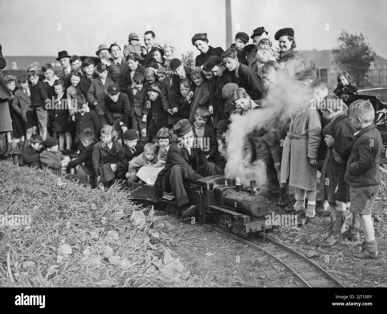 Miniature train. Englishman Jim Haughton has built his own miniature railway and steam locomotive in his garden i the villa Stockport outside Chshire. The picture shows him operating it with children riding in the railway cars behind him. 1944 Stock Photo
