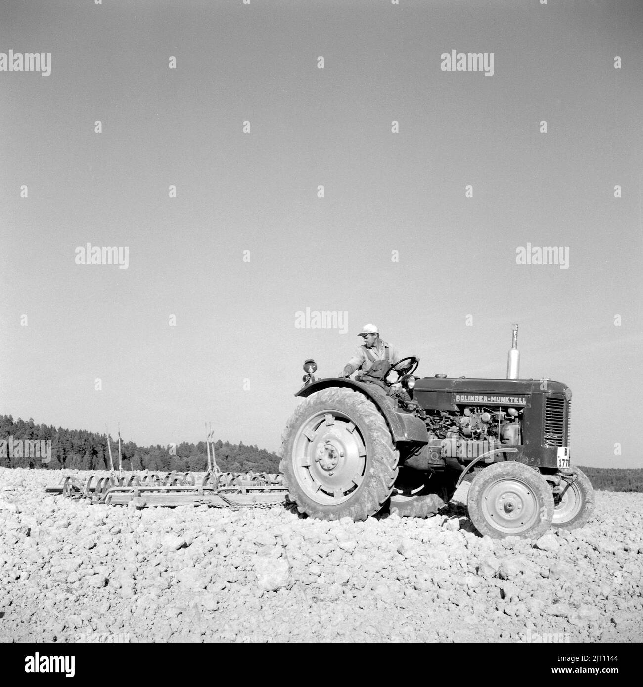 Farming in the 1950s. A Bolinder-Munktell tractor pulls a harrow and prepares the earth for another season of farming. Hamra farm Sweden 1955 Stock Photo