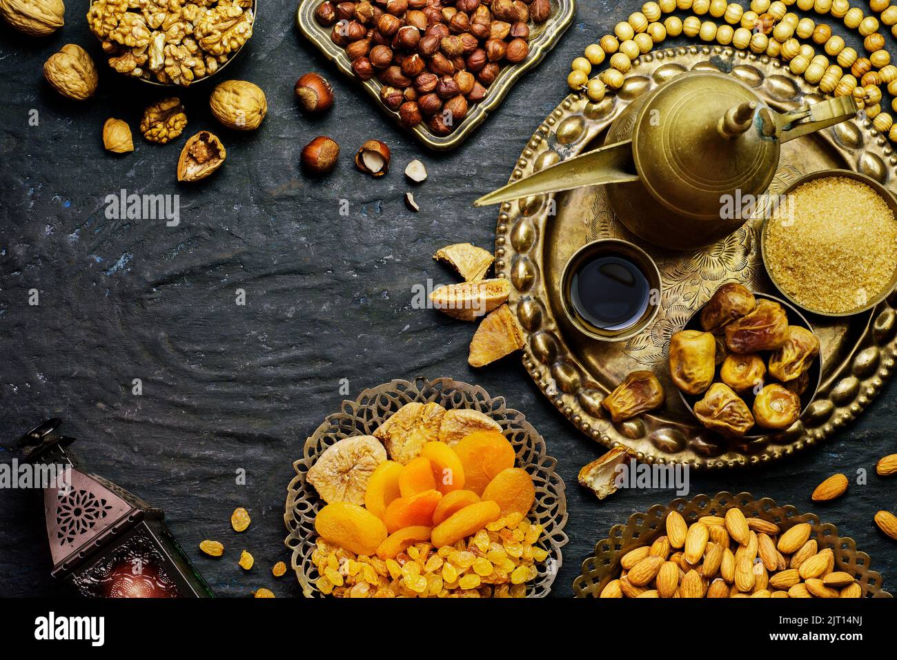 Ramadan concept. Varieties of dried fruits, nuts, Arabian coffee, dates and traditional Ramadan lantern on rustic dark background. Stock Photo