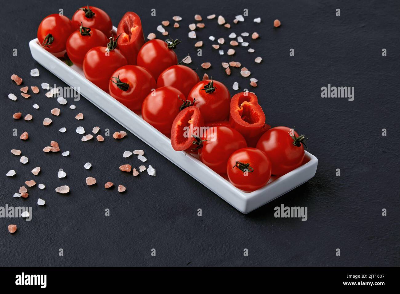 An elongated plate of tomatoes, paprika and coarse pink Tibetan salt on a black concrete table Stock Photo