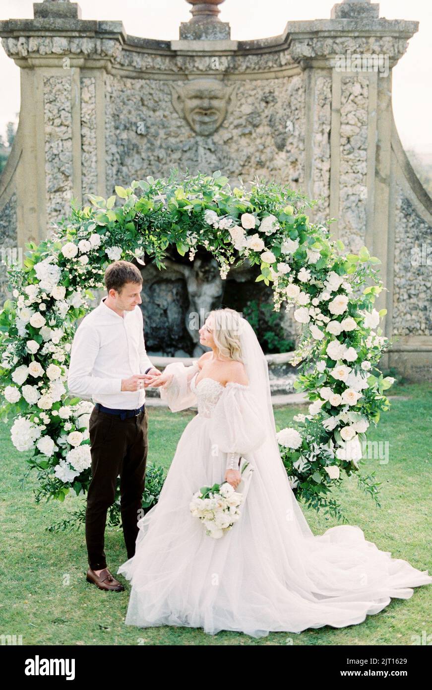Groom puts a ring on the finger of bride in a white dress at the