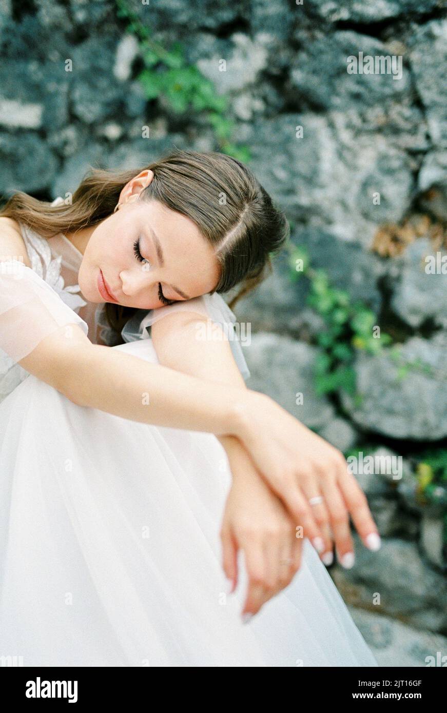 Bride in a white dress sits on stone steps with her head on her knees ...