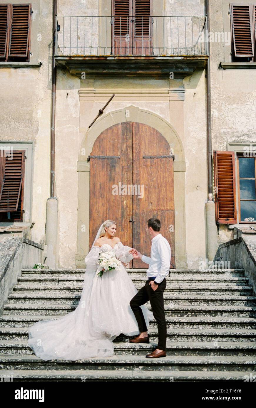 Bride and groom stand on the steps in front of the wooden door of an ...