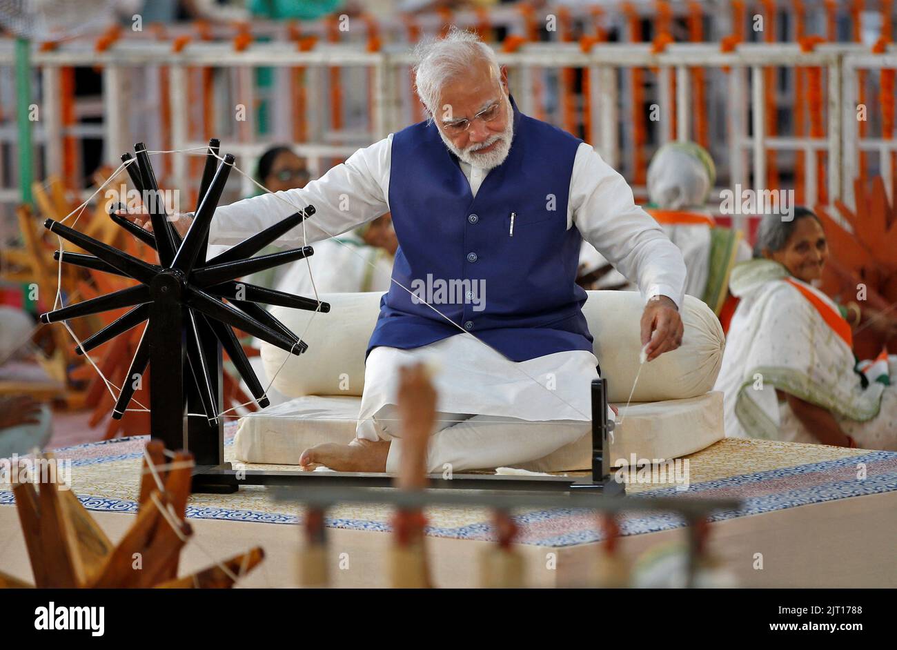 India's Prime Minister Narendra Modi spins cotton on a wheel during an event where 7500 artisans spin cotton live at same place to promote hand woven cotton cloth as part of the celebrations commemorating 75 years of India's Independence, in Ahmedabad, India, August 27, 2022. REUTERS/Amit Dave Stock Photo