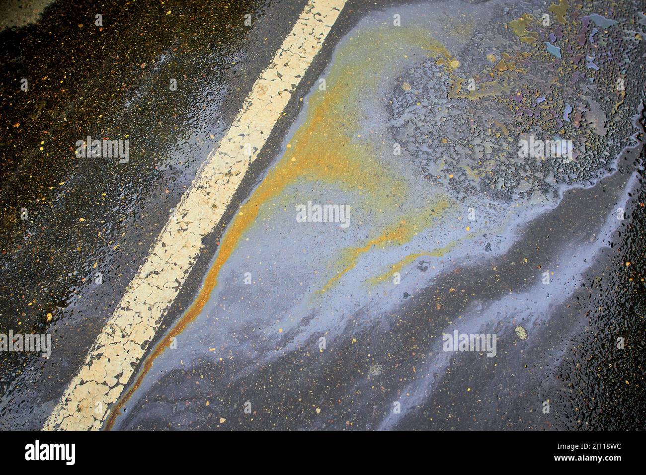 Gasoline spill on asphalt with a white dividing strip in a car park as