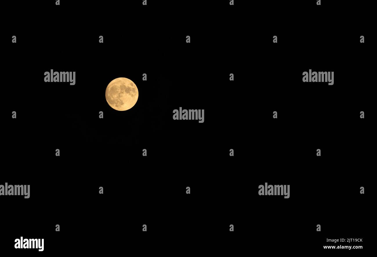 Full moon glows orange against deep black night sky Stock Photo