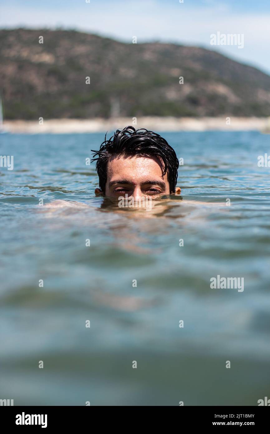 Handsome Caucasian man submerged in water. He is on a beach and you can