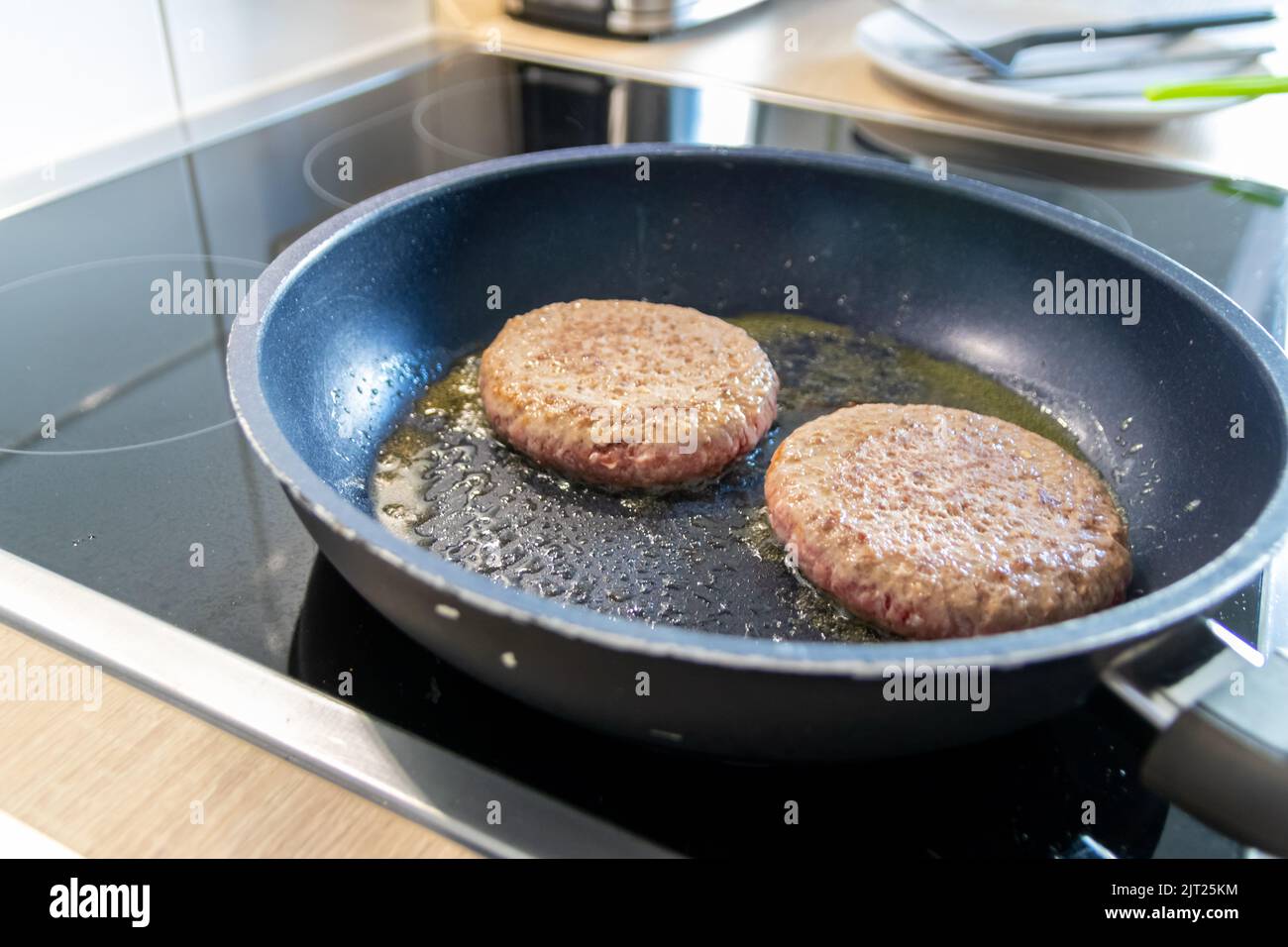 Two burger patties burger meat sizzling in hot pan with fat and oil as delicious selfmade hamburger bbq meatballs as unhealthy fast food lunch Stock Photo