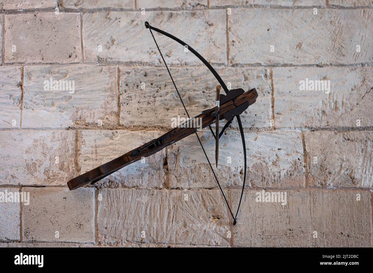 A closeup shot of an ancient crossbow weapon hanging on the stone wall of the castle Stock Photo