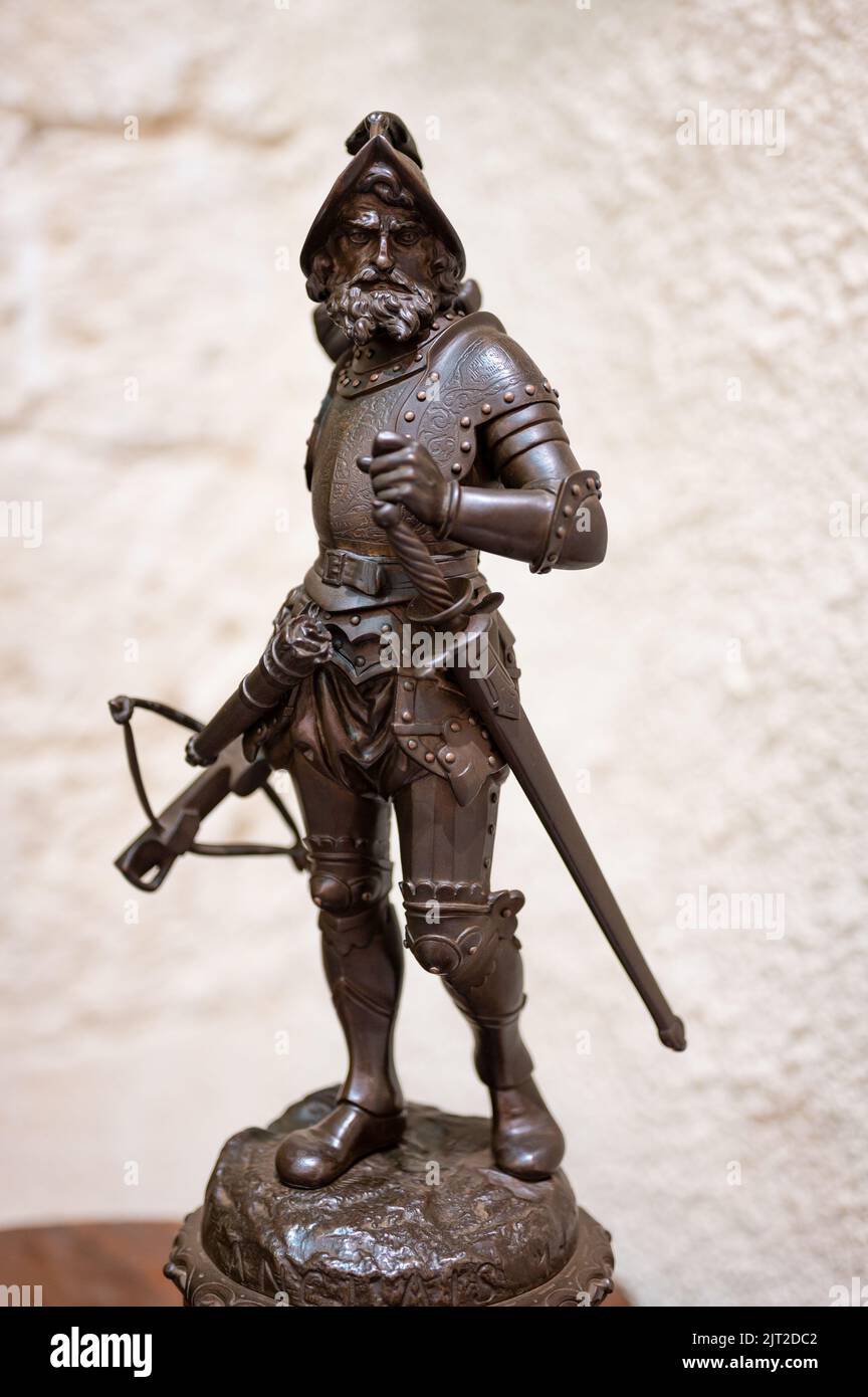 A vertical closeup shot of an old bronze statuette of a warrior soldier with armor, sword, and crossbow Stock Photo