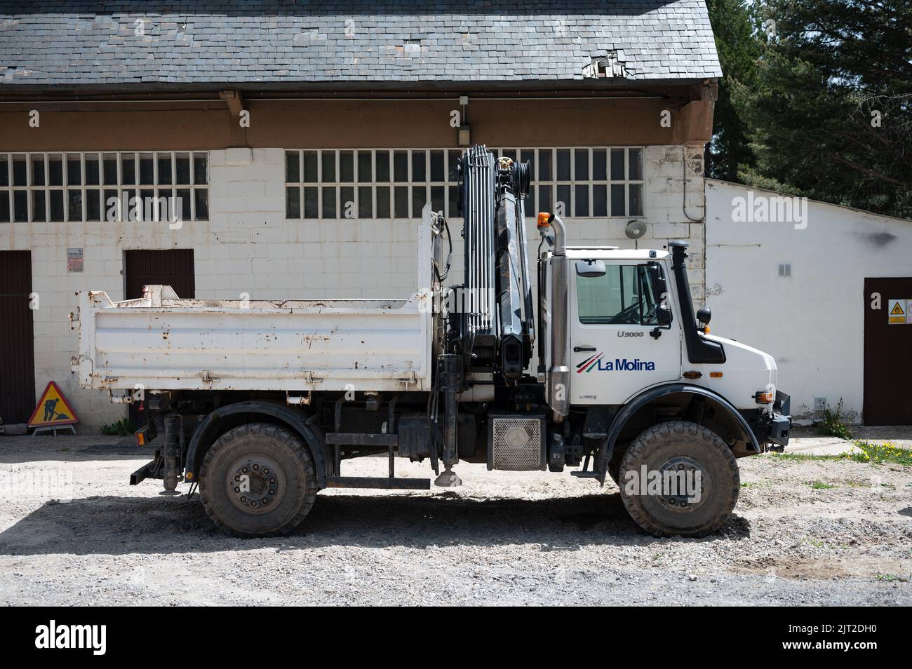 A side view of a white Mercedes Benz Unimog G5000 off-road truck with a crane in front of a building Stock Photo