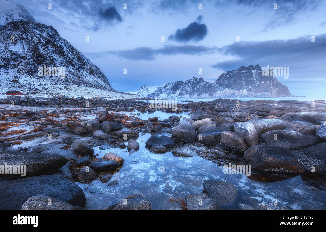 Sea coast with stones and blurred water, snowy rocky mountains Stock Photo