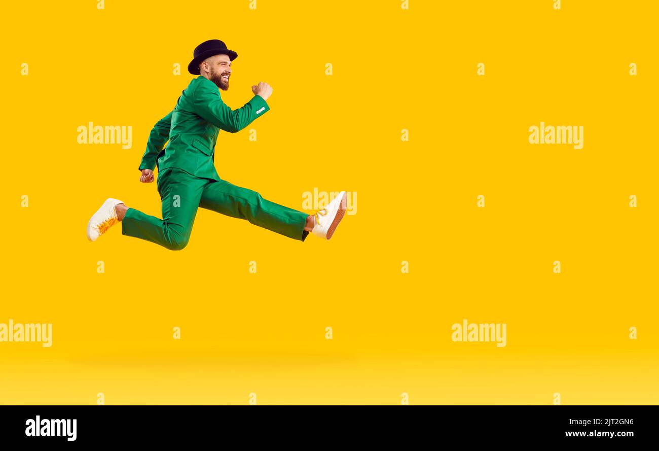Happy man in a green suit hurrying to Patrick's Day and jumping on a yellow copy space background Stock Photo