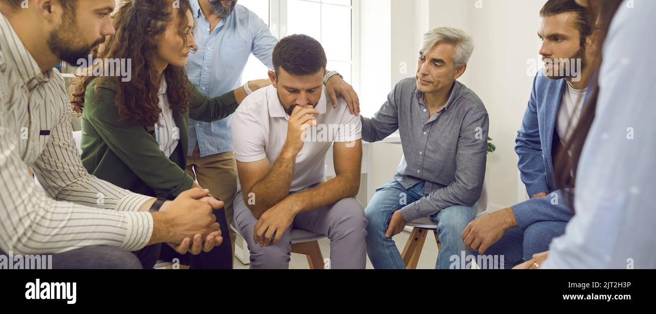 People supporting and comforting a depressed young man during a group therapy session Stock Photo