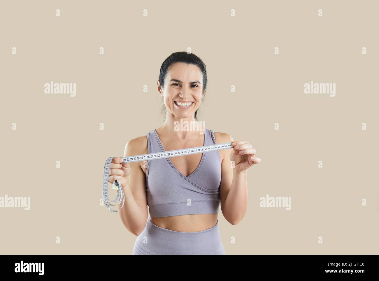 Female sports trainer or fitness instructor holding measuring tape isolated on beige background. Stock Photo