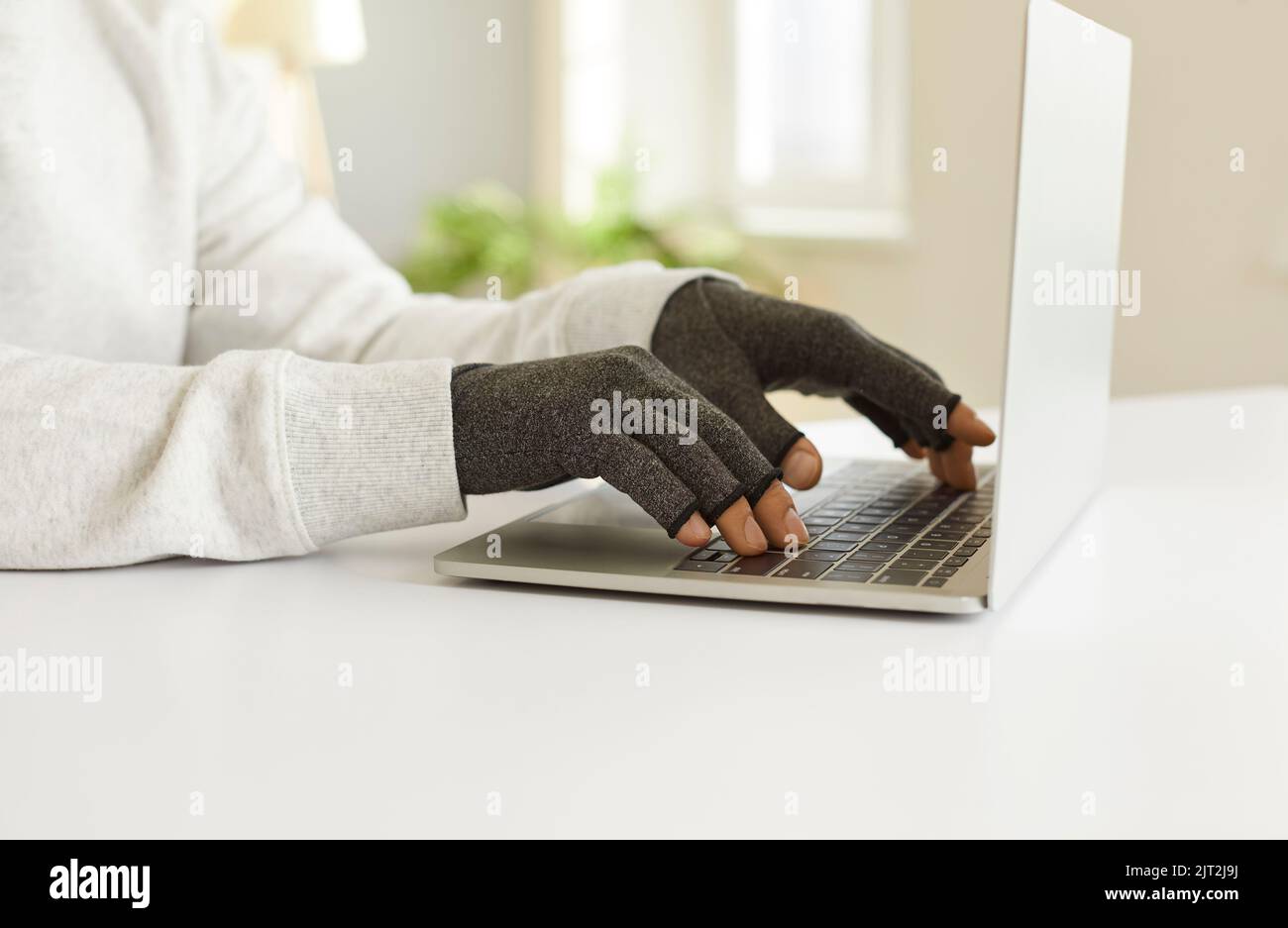 Man with rheumatoid arthritis types text on laptop wearing special compression gloves. Stock Photo