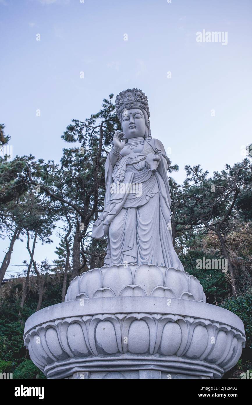 A vertical shot of a Guanyin white stone statue against trees Stock Photo