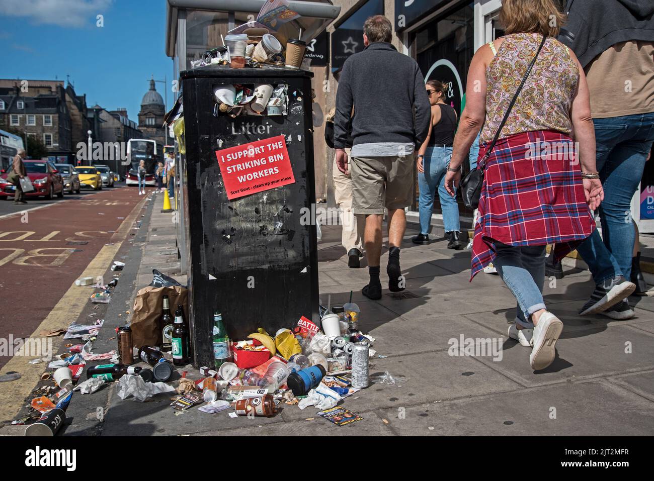 Pedestrians walking by an overflowing rubbish bin on Nicolson Street due to industrial action by Edinburgh council workers. Stock Photo