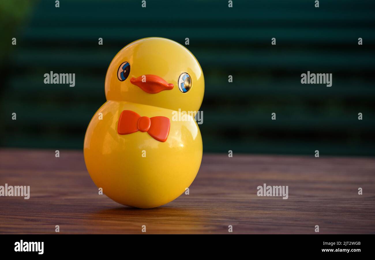 Vintage roly-poly toy shaped like a cute yellow chick. Tumbler toy isolated on an outdoor wooden table at sunset. Stock Photo