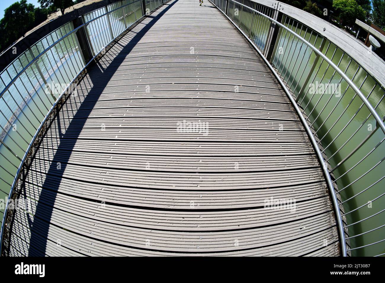 Wooden bridge over aachener weiher in cologne in sunlight with shadow in fisheye perspective Stock Photo