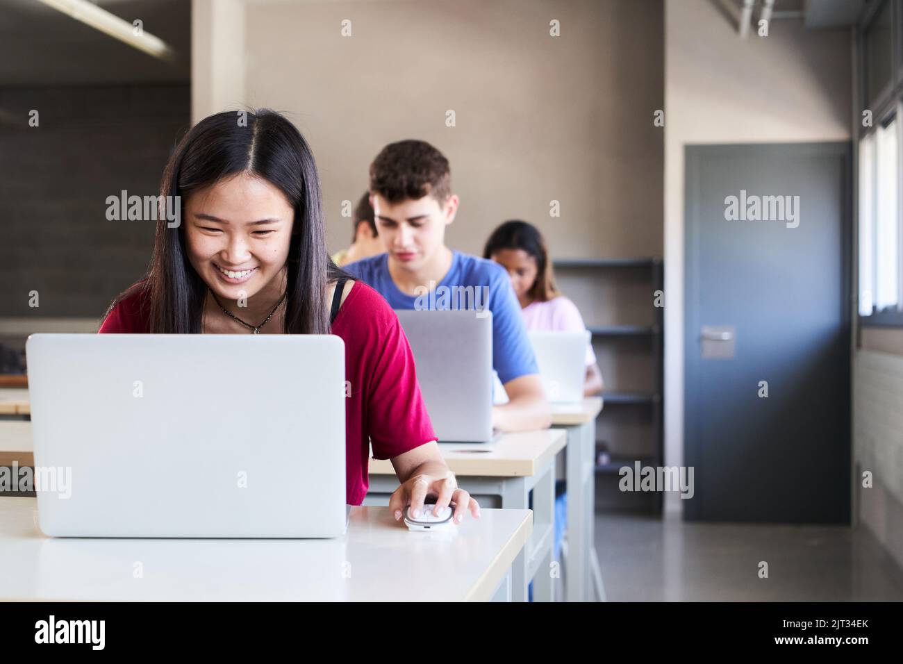 Multiracial group of high school students in the classroom using laptop computers. A smiling Asian girl studies through digital media in new Stock Photo