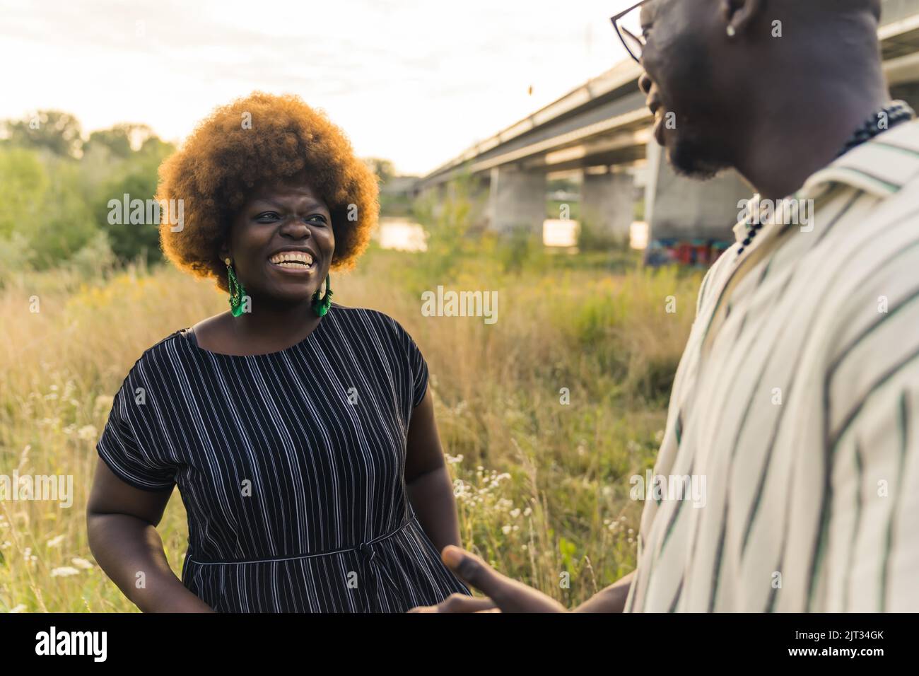 Smiling ethnic dark-skinned straight couple having a relaxing summer evening, talking, laughing and strolling in nature near the river. High quality photo Stock Photo