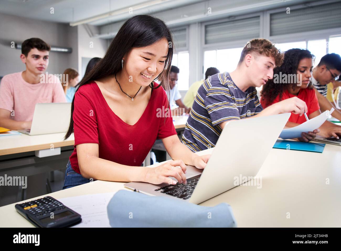 Cheerful Smiling Asian high school student girl using a laptop computer at class. A group of happy classmates in classroom. Education and technology Stock Photo