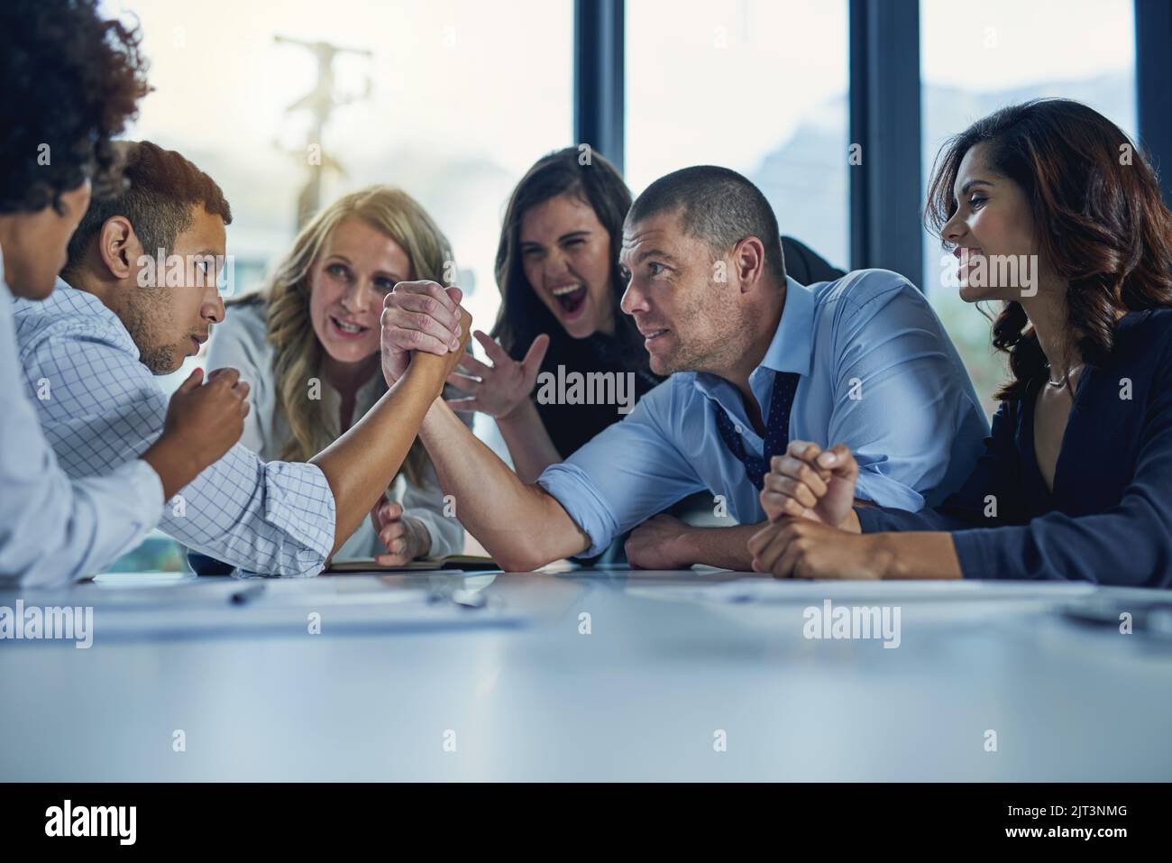 Its a business standoff. two businesspeople arm wrestling during a meeting in the boardroom. Stock Photo