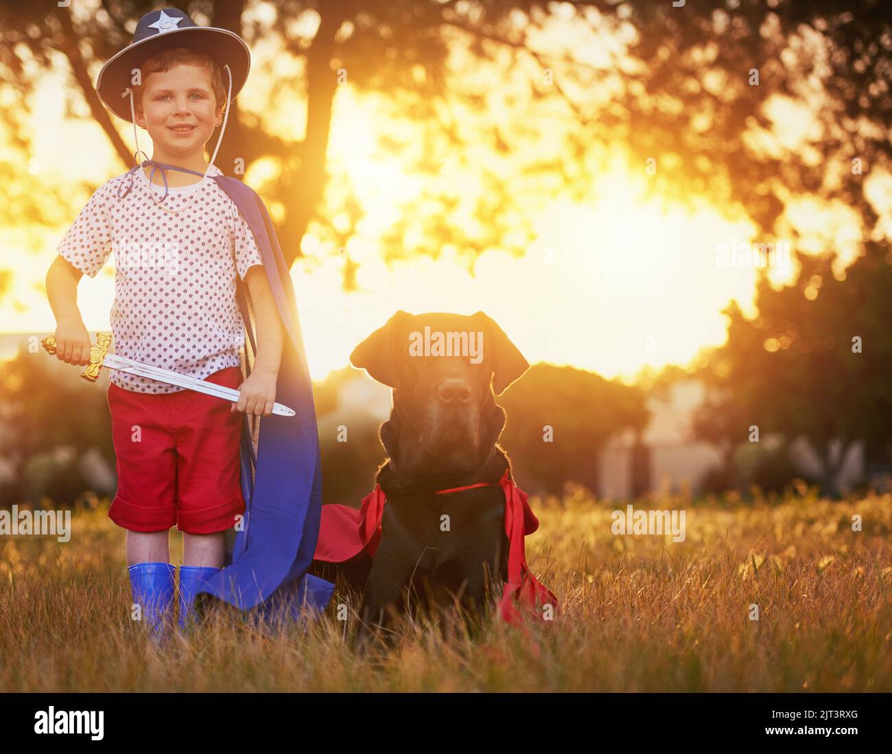 Were here to protect and serve. a little boy and his dog wearing capes while playing outside. Stock Photo