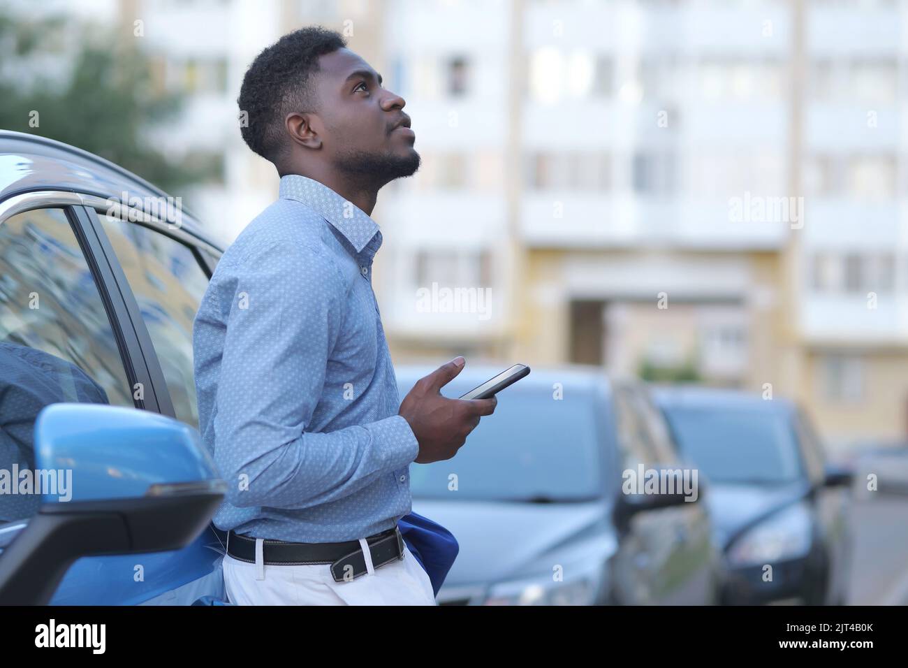 Handsome young businessman using smartphone while standing near his car outdoors, copyspace Stock Photo