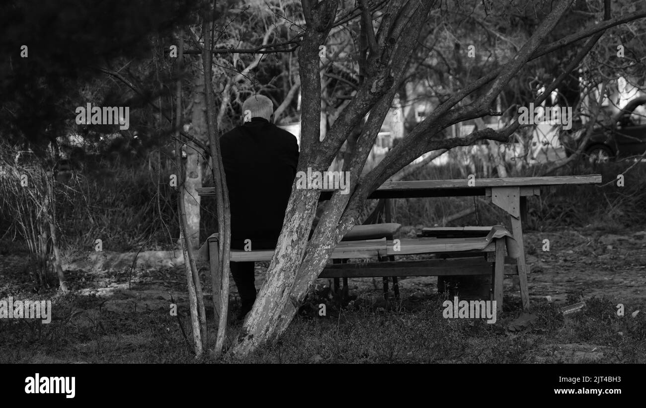 A grayscale shot of a lonely old man sitting on a bench Stock Photo