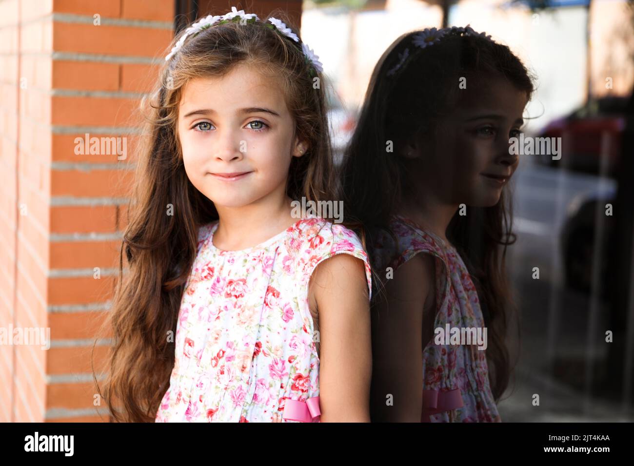 A pretty little girl leaning against a glass window while posing
