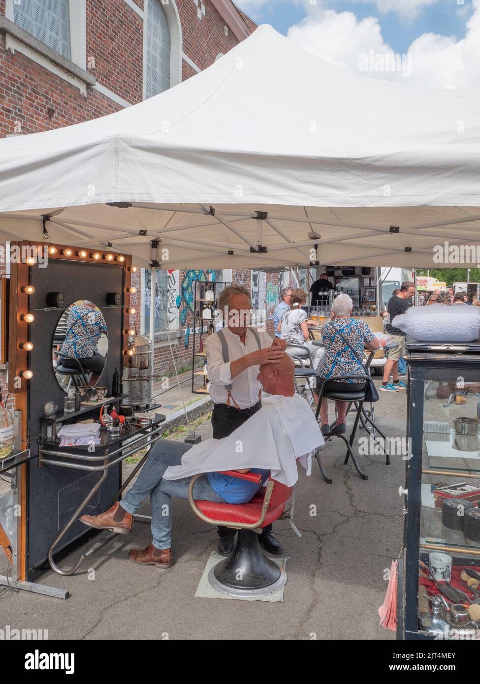 Sint Gillis Waas, Belgium, 21 August 2022, Elderly barber shaves a man's head during a street fair Stock Photo