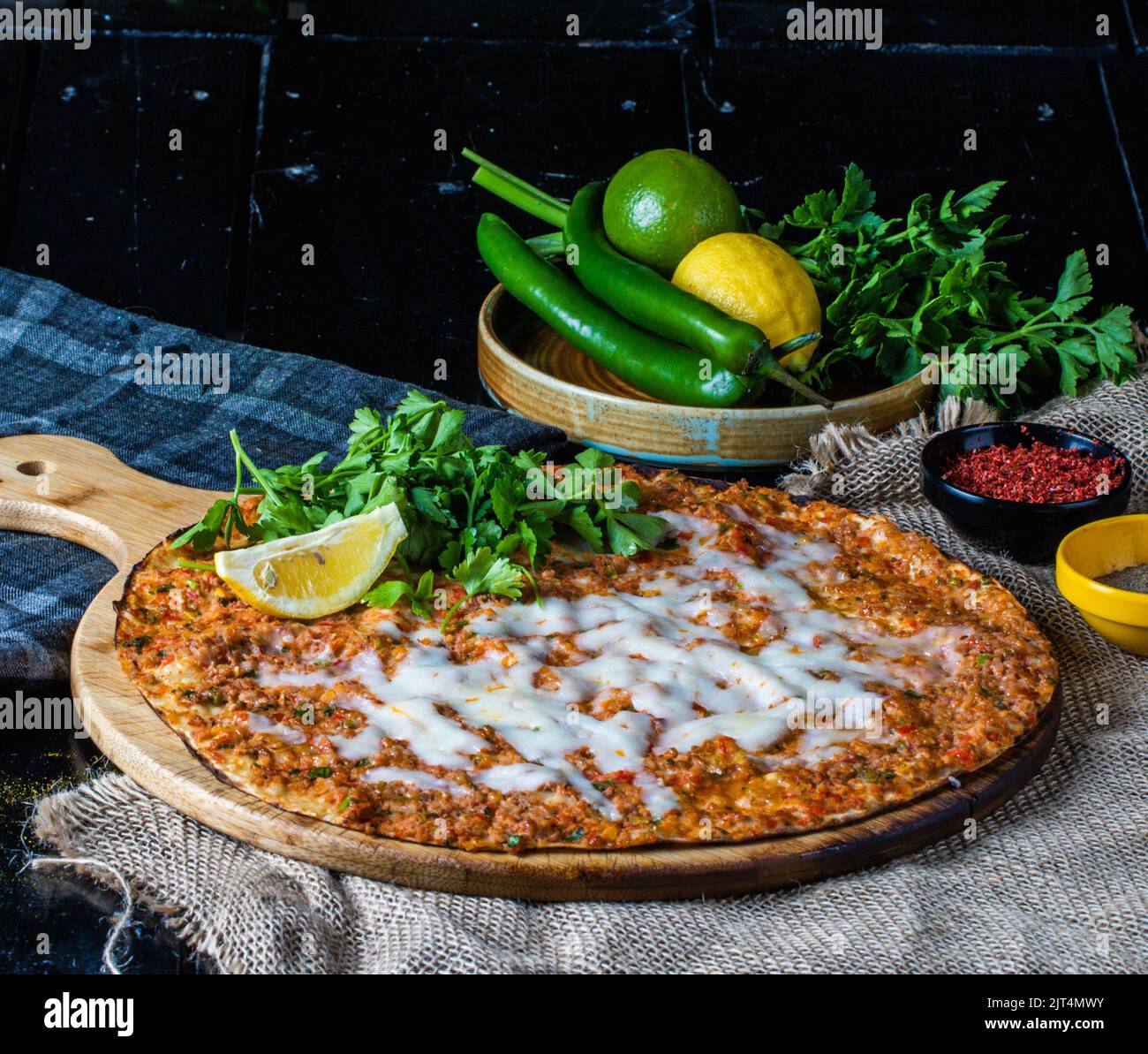 A tasty pizza with fresh herbs on a wooden tray alongside chilies