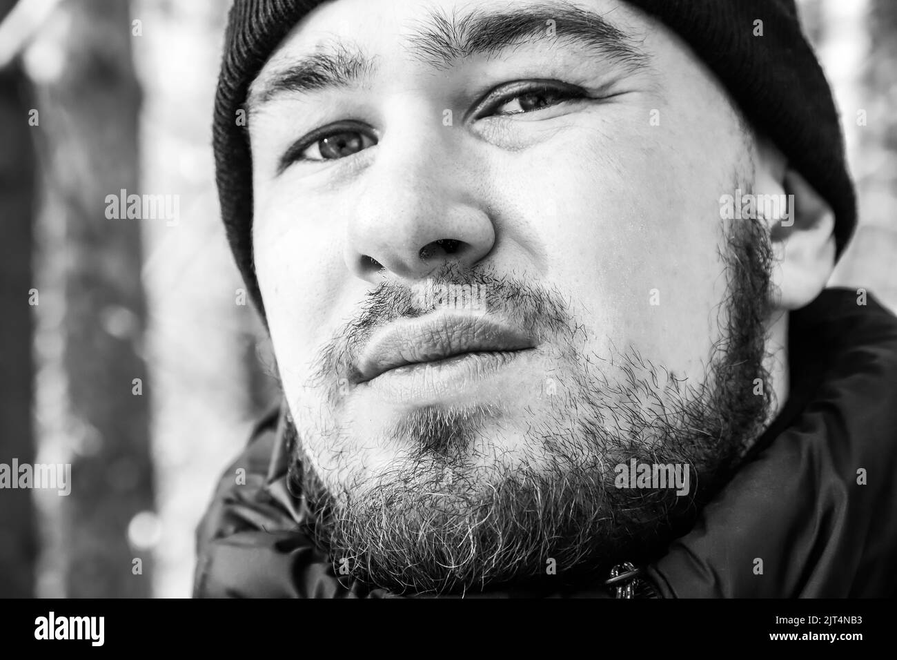 Face of a young man with beard and moustache close-up. Black and white. Selective focus. Outdoors Stock Photo