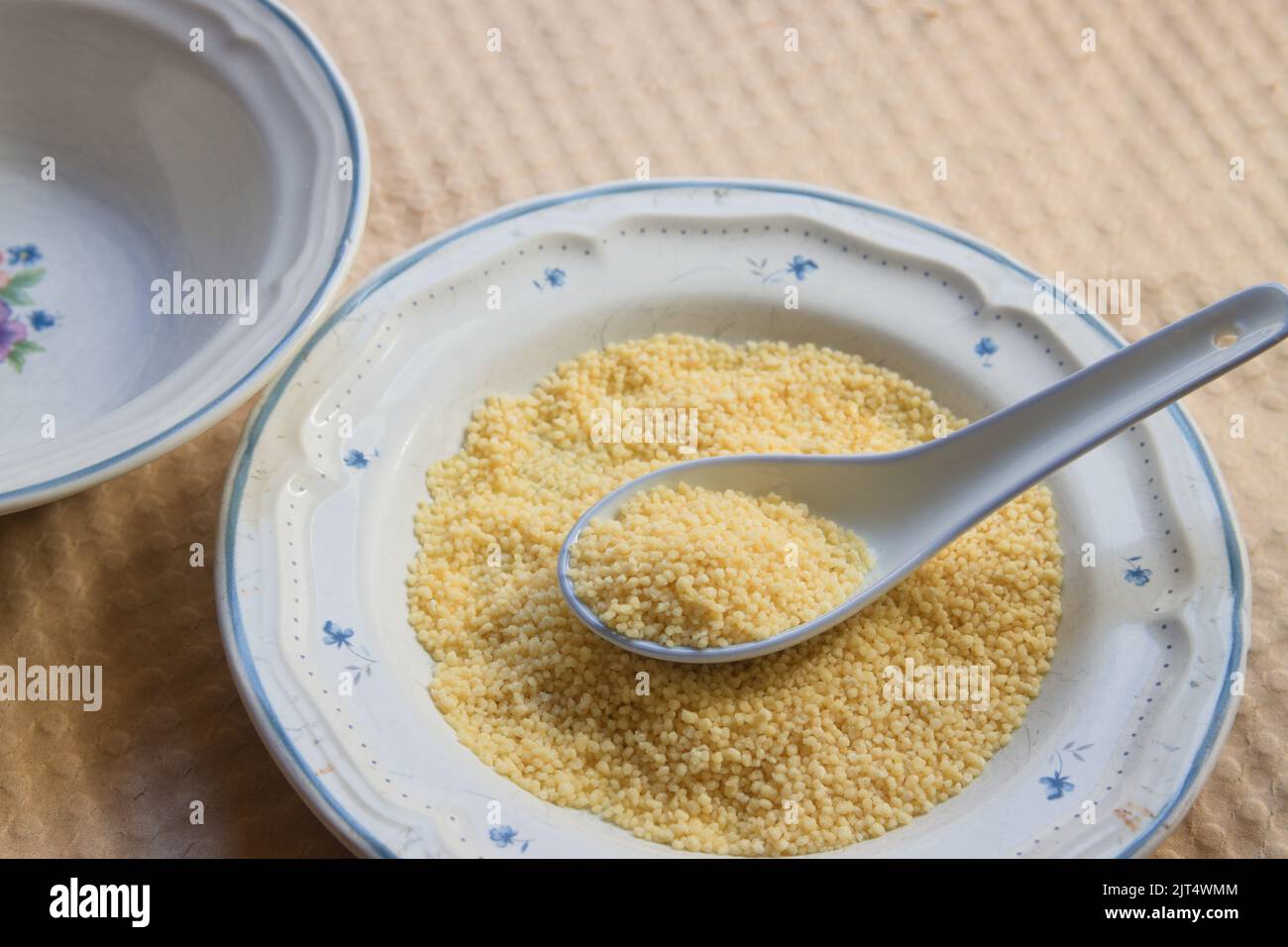 Image of a plate in which there is some raw semolina with a porcelain spoon on a cardboard surface Stock Photo