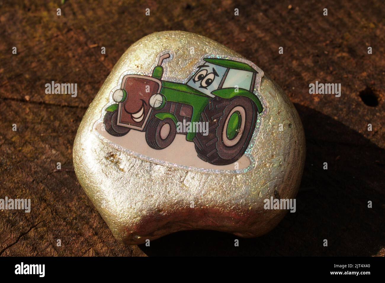 A close up of a stone, pebble, painting of a child's charactor tractor with a face Stock Photo