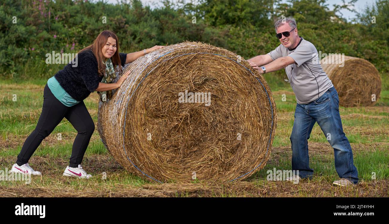 Funny teamwork concept, playing with a large roll of hay in a field, in Ireland. Stock Photo