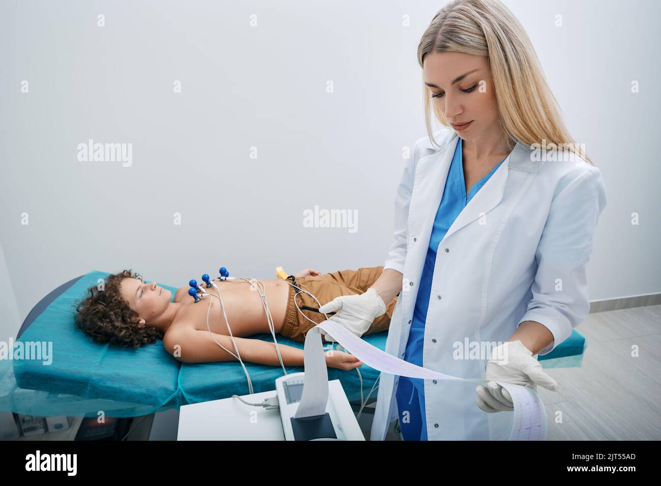 Pediatrician looking ECG printout of child patient after heart electrocardiogram procedure at medical clinic Stock Photo