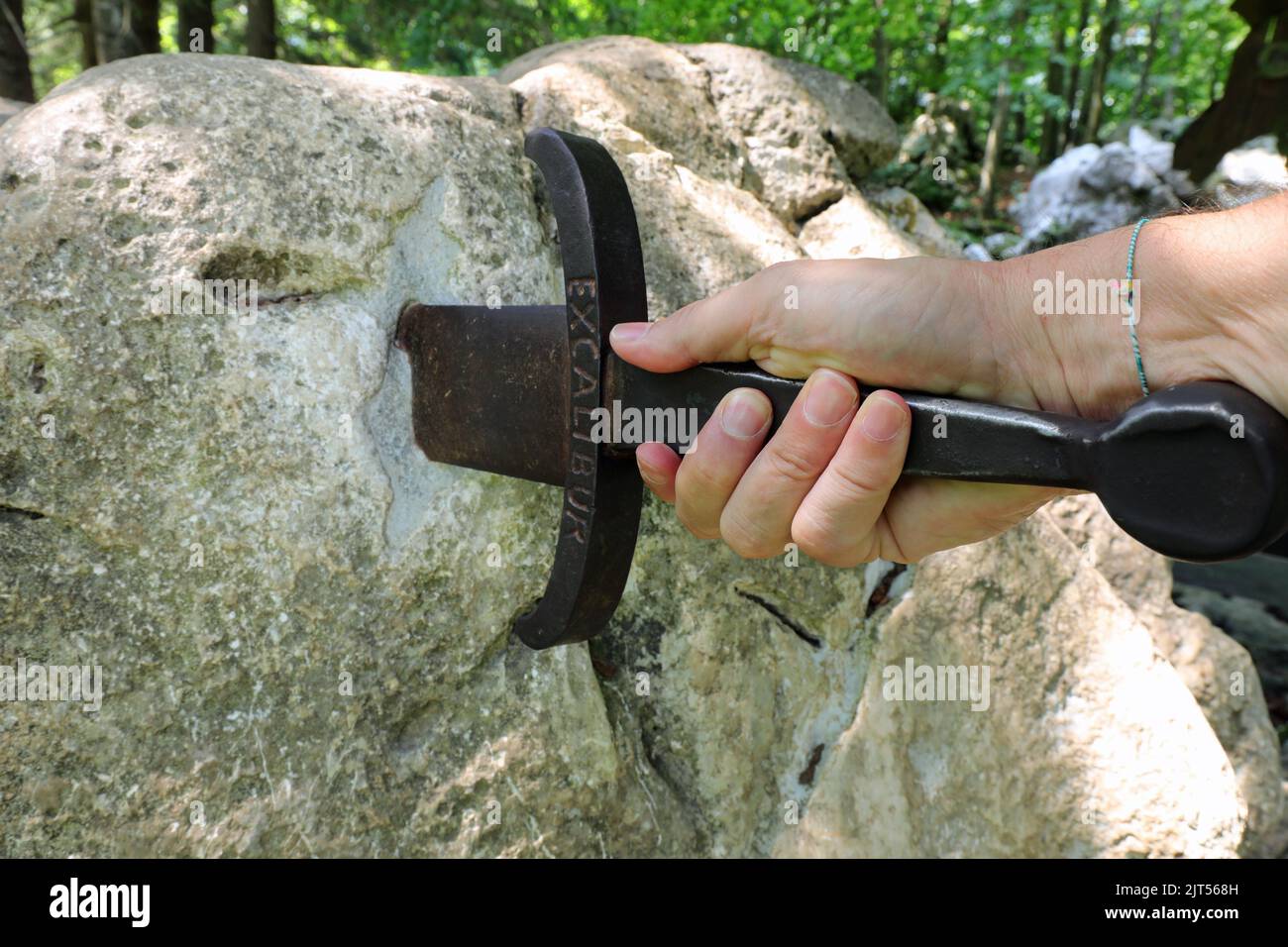 Hand grabbing the sword with the inscription Excalibur stuck on the rock as in the legend of King Arthur Stock Photo