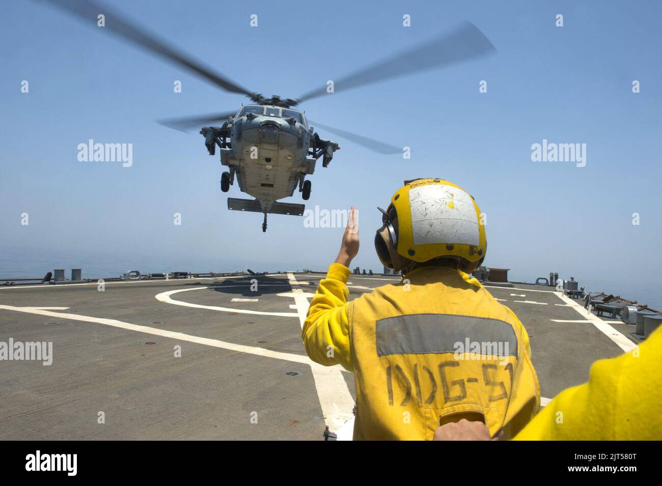 U.S. Navy Lt. j.g. signals an MH-60S Seahawk helicopter attached to Helicopter Sea Combat Squadron (HSC) 9 to land on the guided missile destroyer USS Arleigh Burke (DDG 51) in the Persian Gulf 140628 Stock Photo