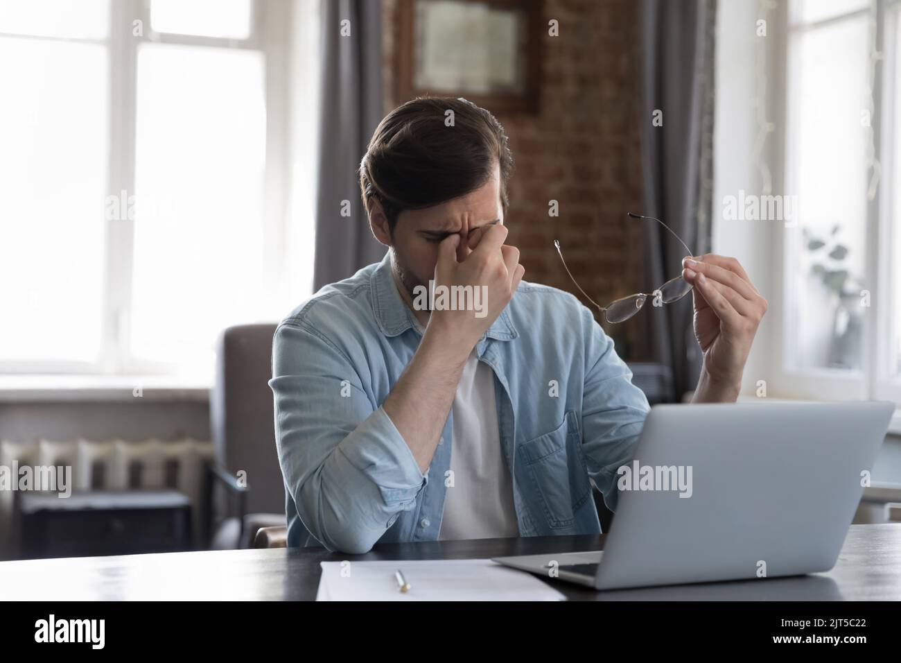 Tired millennial businessman sitting at laptop, rubbing eye lids Stock Photo